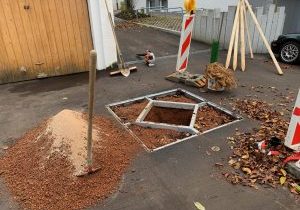 Pflanzgrube mit Baumscheibenrahmen, Substrat und Spaten auf einer Parkfläche