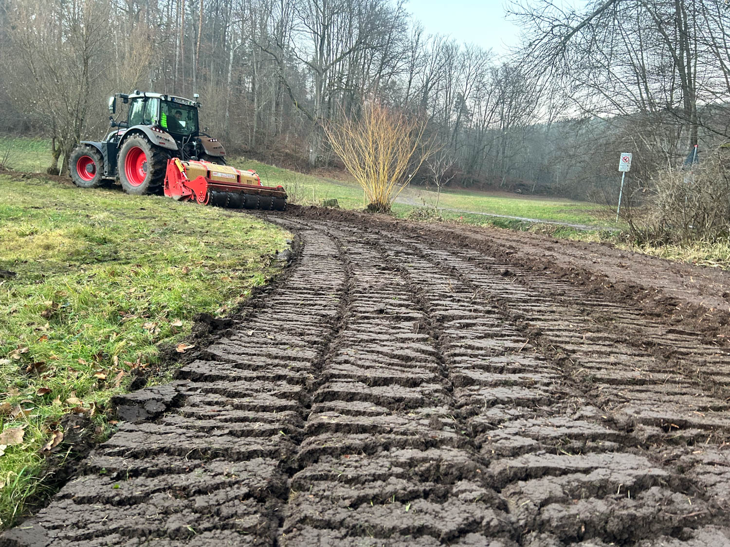 Traktor mit Forstmulcher auf einer frisch gemulchten Fläche am Waldrand