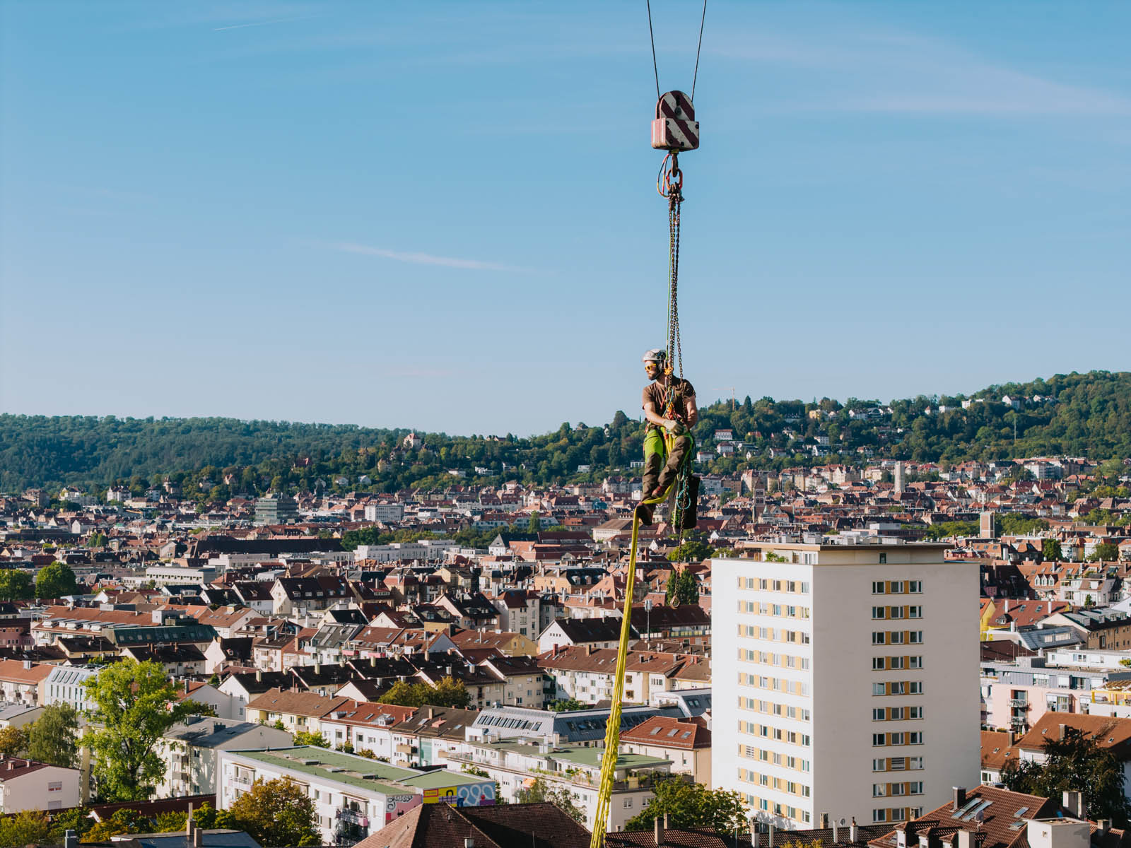 Baumkletterer am Kranseil bei einer Kranfällung hoch über den Dächern von Stuttgart